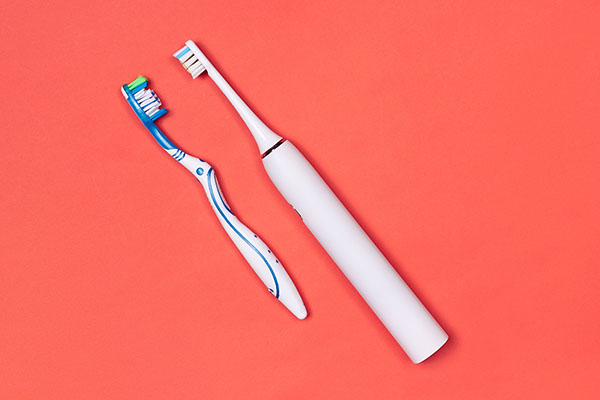 Manual and electric toothbrushes on pink coral background. Denta